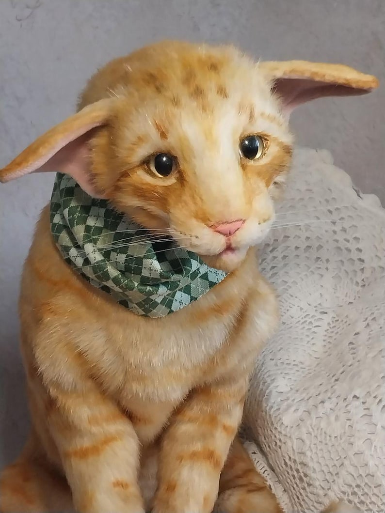 Realistic soft stuffed orange tabby Oriental breed cat toy has yellow taxidermy eyes, pink colored polymer clay paws, white translucent polymer clay claws, and artificial whiskers. The cat  has a green scarf with a diamond pattern. Perfect for collectors, gifts, memorial pet, and home decor.