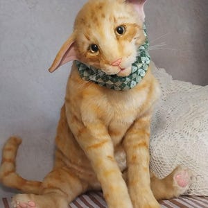 Realistic soft stuffed orange tabby Oriental breed cat toy has yellow taxidermy eyes, pink colored polymer clay paws, white translucent polymer clay claws, and artificial whiskers. The cat  has a green scarf with a diamond pattern. Perfect for collectors, gifts, memorial pet, and home decor.