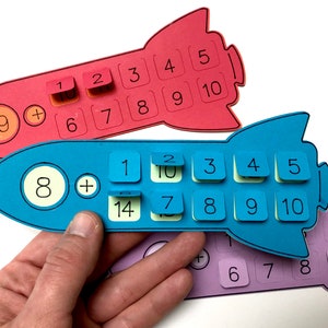 May include: Three colorful rocket-shaped counting manipulatives with numbers 1 through 10 on each. The rockets are red, blue, and purple. The numbers are printed in black. The rockets are used for teaching math concepts.