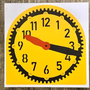 May include: A yellow clock face with black numbers and a black gear-shaped border. The hour hand is red and the minute hand is black. The clock face has numbers from 1 to 12 and numbers from 5 to 60 around the edge.