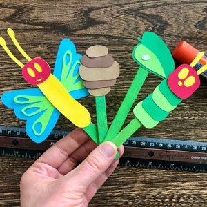 May include: A craft project featuring a butterfly, caterpillar, and honeycomb made from paper and attached to wooden sticks.