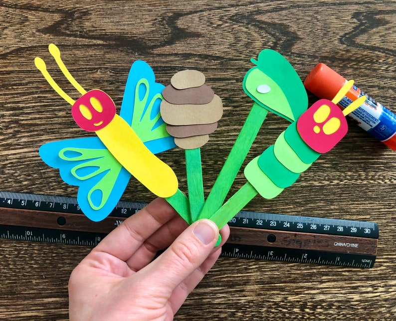 May include: A craft project featuring a butterfly, caterpillar, and honeycomb made from paper and attached to wooden sticks.