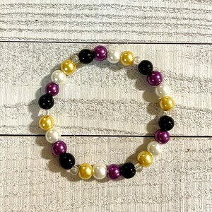 May include: A beaded bracelet with black, white, gold, and purple beads.