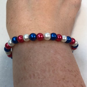May include: A red, white, and blue beaded bracelet. The bracelet is made with small, round beads in a patriotic color scheme.