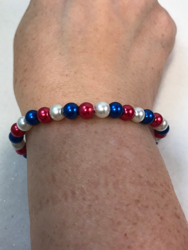 May include: A red, white, and blue beaded bracelet. The bracelet is made with small, round beads in a patriotic color scheme.
