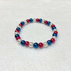 May include: A white, blue, and red beaded bracelet. The beads are arranged in a repeating pattern.