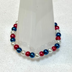 May include: A bracelet made of white, red, and blue beads. The beads are arranged in a repeating pattern.