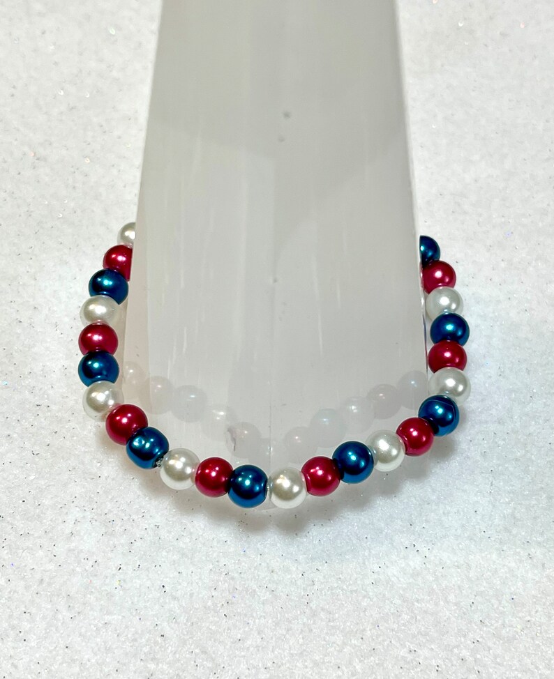 May include: A bracelet made of white, red, and blue beads. The beads are arranged in a repeating pattern.