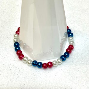 May include: A red, white, and blue beaded bracelet. The beads are arranged in a pattern of red, white, and blue.