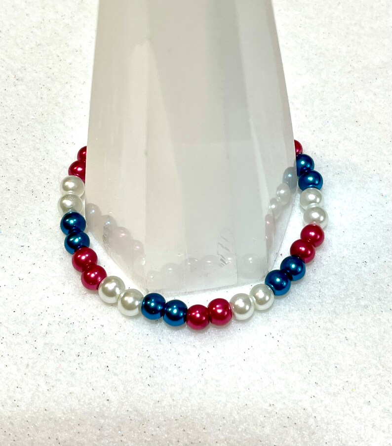 May include: A red, white, and blue beaded bracelet. The beads are arranged in a pattern of red, white, and blue.