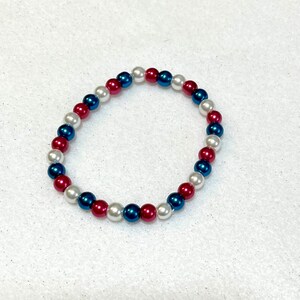 May include: A bracelet made of white, blue, and red beads. The beads are arranged in a repeating pattern.