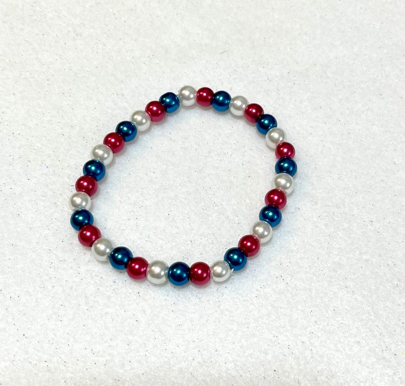 May include: A bracelet made of white, blue, and red beads. The beads are arranged in a repeating pattern.