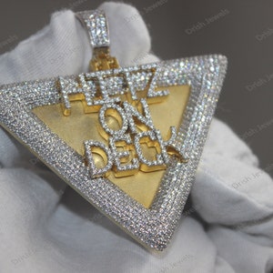 May include: A gold and silver triangle pendant with the words "Here On Deck" set in diamonds.