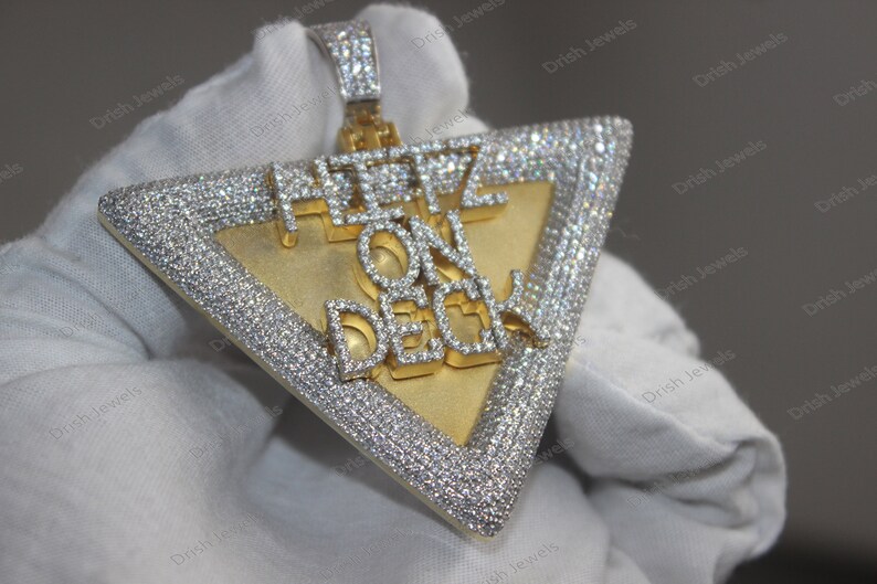 May include: A gold and silver triangle pendant with the words "Here On Deck" set in diamonds.