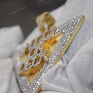 May include: A gold pendant with a geometric design, fully encrusted with clear cubic zirconia stones. The pendant is on a white surface.