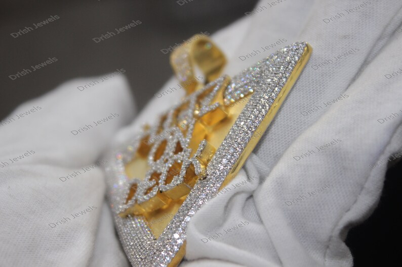May include: A gold pendant with a geometric design, fully encrusted with clear cubic zirconia stones. The pendant is on a white surface.