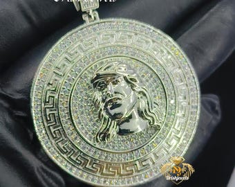 May include: Silver pendant necklace with a round, silver, and clear crystal-encrusted design featuring a face of Jesus Christ. The pendant is surrounded by a Greek key pattern. The necklace is on a silver chain.