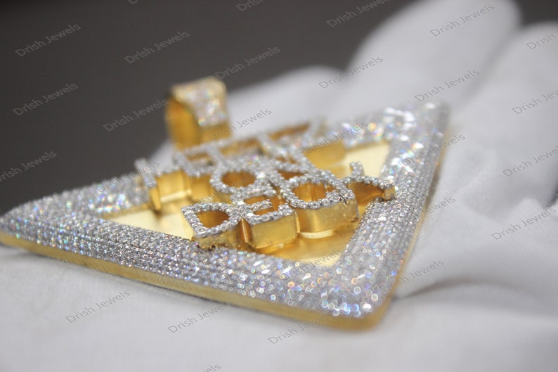 May include: A gold pendant with the words "ICE COLD" set in diamonds. The pendant is shaped like a triangle and has a diamond-encrusted border.