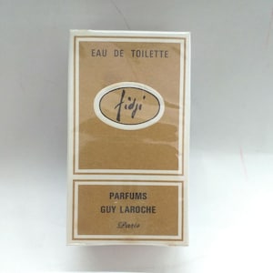 May include: A brown and white box with the text "Eau de Toilette" and "Parfums Guy Laroche Paris" on it. The box has a white oval with the word "Fidji" in black script inside.