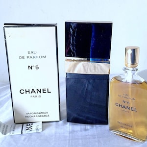 Puede incluir: Un frasco negro y dorado de Chanel No. 5 Eau de Parfum con un atomizador recargable. El frasco est&aacute; etiquetado con "Eau de Parfum N&deg;5 Chanel Paris" y "Recharge Refill 1.2 fl oz 35 ml".