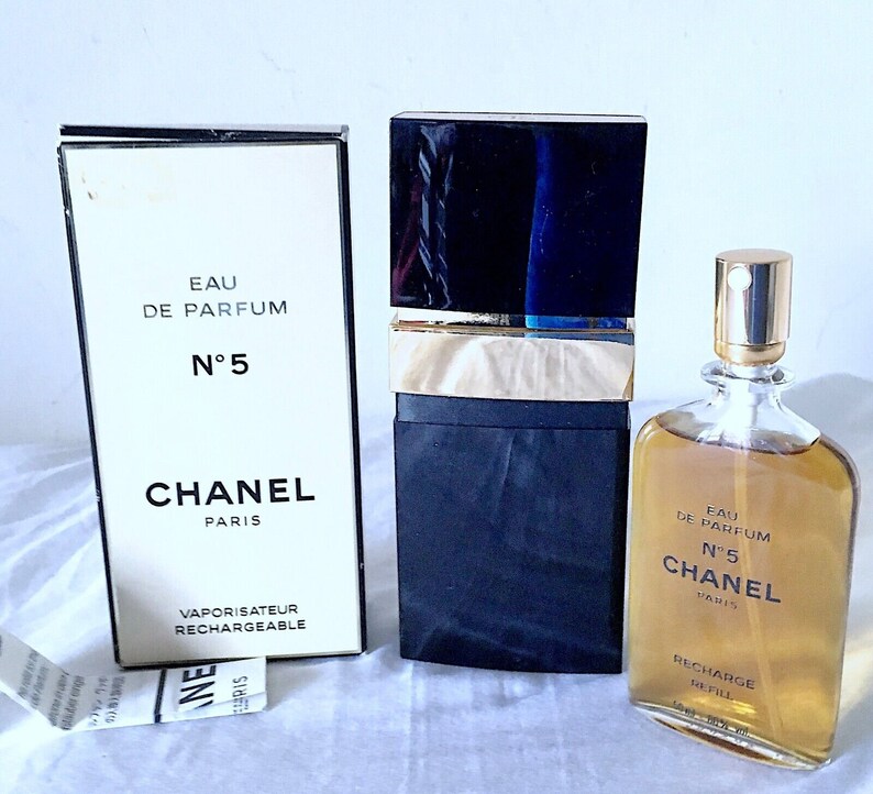 Puede incluir: Un frasco negro y dorado de Chanel No. 5 Eau de Parfum con un atomizador recargable. El frasco est&aacute; etiquetado con "Eau de Parfum N&deg;5 Chanel Paris" y "Recharge Refill 1.2 fl oz 35 ml".