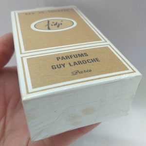 May include: A brown cardboard box with white trim, featuring the text "PARFUMS GUY LAROCHE Paris" and a logo with the word "Fidji" in a circle. The box is wrapped in clear plastic.