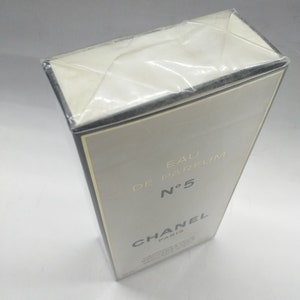 Puede incluir: Una caja blanca con bordes negros y letras doradas. La caja es para Chanel N&deg;5 Eau de Parfum.