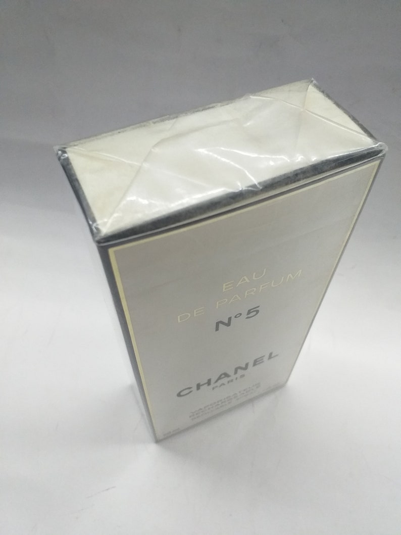 Puede incluir: Una caja blanca con bordes negros y letras doradas. La caja es para Chanel N&deg;5 Eau de Parfum.