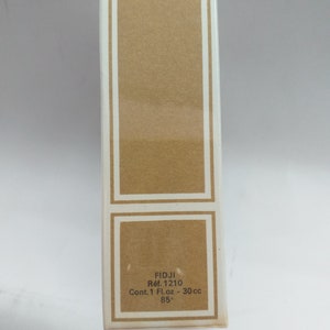 May include: A white box with a brown label. The label says "FIDJI R&eacute;f. 1210 Cont. 1 Fl. oz - 30 cc 85&deg;".