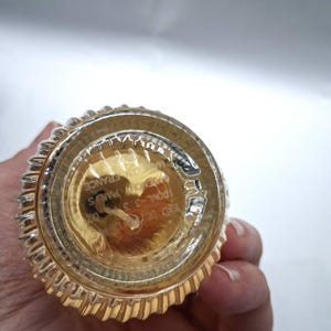 May include: Bottom view of a perfume bottle with a gold-colored base and a ribbed, silver-colored rim. The bottle has text that reads "GIVENCHY PARIS FRANCE" and "100ML-3.3 FL.OZ."