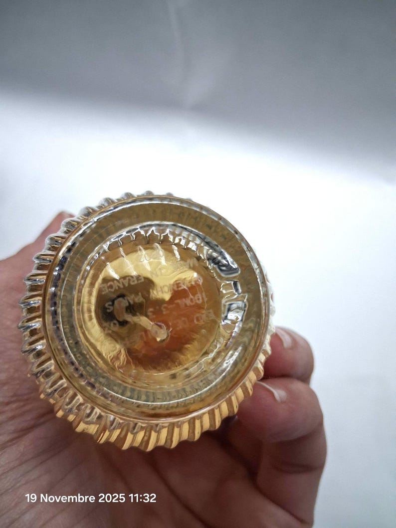 May include: Bottom view of a perfume bottle with a gold-colored base and a ribbed, silver-colored rim. The bottle has text that reads "GIVENCHY PARIS FRANCE" and "100ML-3.3 FL.OZ."