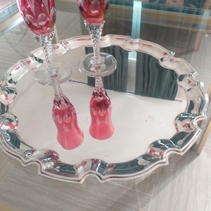 May include: Two red stemmed glasses with etched designs sit on a silver serving tray with a scalloped edge.