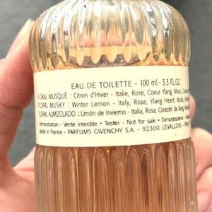 May include: A clear glass bottle of Eau de Toilette, 100 ml (3.3 fl oz), with a silver cap. The bottle has a ribbed design and contains a light amber liquid. Text on the label includes fragrance notes and the brand name.