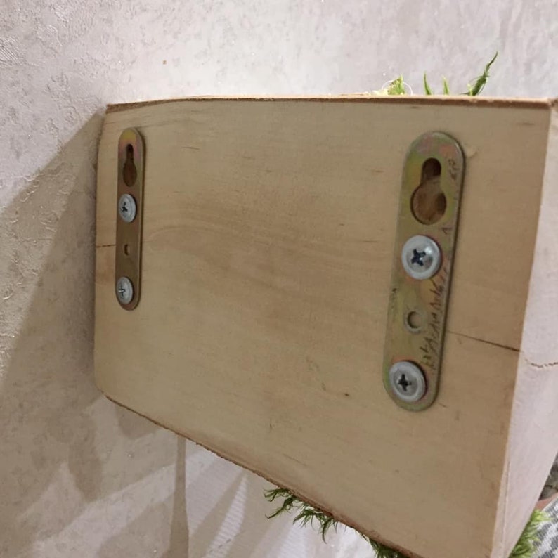 Puede incluir: La parte posterior de una estanter&iacute;a de madera con dos soportes met&aacute;licos unidos. Los soportes tienen tornillos y un agujero para colgar. La estanter&iacute;a est&aacute; sin terminar y tiene un color de madera natural.