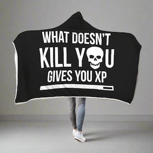 May include: Black hooded blanket with white text that reads "What doesn't kill you gives you XP" and a skull graphic.
