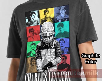 Peut inclure: Un t-shirt gris graphite avec un graphique central représentant un pilote de course portant un casque, entouré d'une grille de huit portraits plus petits du même pilote dans diverses couleurs. Le texte "CHARLES LECLERC THE ERAS TOUR" est imprimé en dessous.
