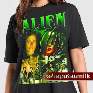 May include: Black t-shirt with a green and white graphic print of the movie "Alien" from 1979. The graphic features the alien creature, Ripley, and other characters from the film.