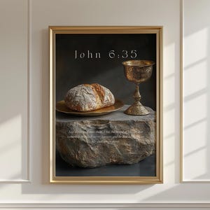 Puede incluir: Impresión enmarcada con una naturaleza muerta que muestra pan sobre un plato dorado, un cáliz dorado y una superficie de piedra. El texto "John 6:35" está en la parte superior. La impresión tiene un marco dorado y está en una pared blanca.
