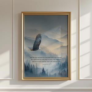 Puede incluir: Impresión enmarcada con marco dorado, que representa un águila volando sobre un paisaje montañoso brumoso. La obra de arte incluye texto de Isaías 40:31. Los colores dominantes son el azul, el gris y el blanco.