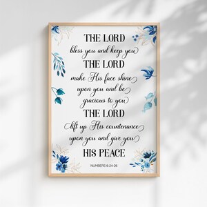 Könnte beinhalten: Ein gerahmter Druck mit einem hellen Holzrahmen. Der Text lautet "THE LORD bless you and keep you...HIS PEACE" in eleganter Schrift. Florale Aquarellakzente in Blau und Gold verzieren die Ecken und Kanten. Der Bibelvers Numeri 6:24-26 steht unten.