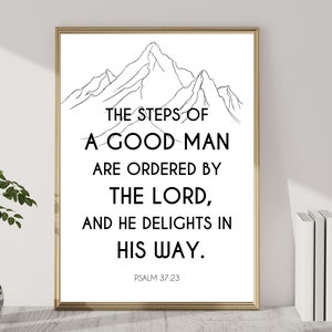 May include: A framed print with a gold border. The white background features black text that reads "THE STEPS OF A GOOD MAN ARE ORDERED BY THE LORD, AND HE DELIGHTS IN HIS WAY. PSALM 37:23." A black and white mountain illustration is at the top.