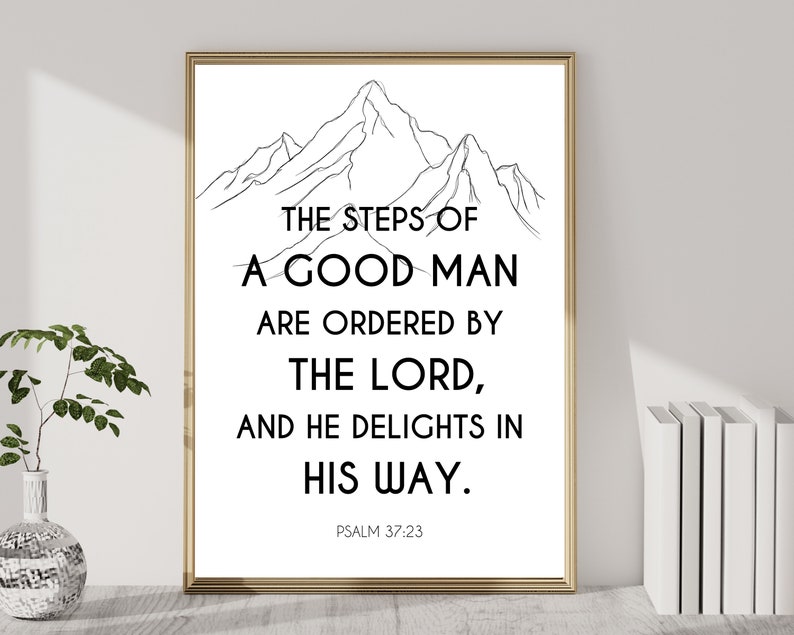 May include: A framed print with a gold border. The white background features black text that reads "THE STEPS OF A GOOD MAN ARE ORDERED BY THE LORD, AND HE DELIGHTS IN HIS WAY. PSALM 37:23." A black and white mountain illustration is at the top.