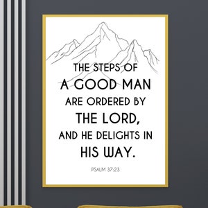 May include: A framed print with a white background and black text. The text reads "THE STEPS OF A GOOD MAN ARE ORDERED BY THE LORD, AND HE DELIGHTS IN HIS WAY." A mountain range illustration is at the top. Psalm 37:23 is at the bottom.