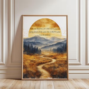 Op de afbeelding: Een ingelijste kunstdruk met een landschap met een kronkelend pad door gouden velden, een donker bos en blauwe bergen onder een grote gele zon. De tekst luidt: From the RISING OF THE SUN unto the going down of the same the LORD'S name is to be praised. Psalm 113:3.