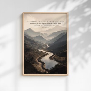 Puede incluir: Una impresión enmarcada de un paisaje con un río sinuoso que fluye a través de un valle rodeado de montañas. La impresión tiene un marco de madera clara e incluye texto de Isaías 58:11. Una escena natural serena.