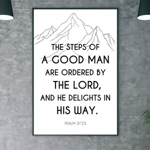 May include: Black framed wall art featuring the text "THE STEPS OF A GOOD MAN ARE ORDERED BY THE LORD, AND HE DELIGHTS IN HIS WAY." Psalm 37:23 is printed below the text. A mountain range is drawn above the text.