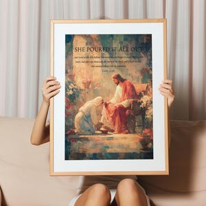 May include: Framed art print featuring a religious scene with the text "SHE POURED IT ALL OUT" and a Bible verse. The artwork depicts a figure kneeling before another, with warm, earthy tones and a soft, painterly style. The frame is a light wood color.