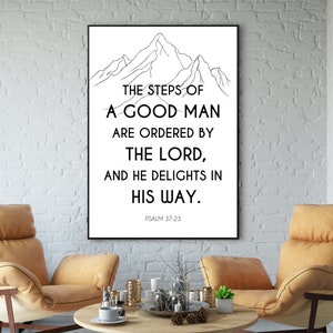 May include: A framed print featuring a mountain outline and the text "THE STEPS OF A GOOD MAN ARE ORDERED BY THE LORD, AND HE DELIGHTS IN HIS WAY." Psalm 37:23 is printed below. The artwork is displayed in a room with two chairs and a coffee table.