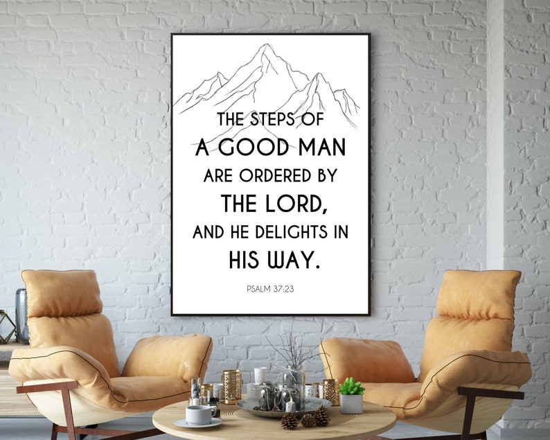 May include: A framed print featuring a mountain outline and the text "THE STEPS OF A GOOD MAN ARE ORDERED BY THE LORD, AND HE DELIGHTS IN HIS WAY." Psalm 37:23 is printed below. The artwork is displayed in a room with two chairs and a coffee table.