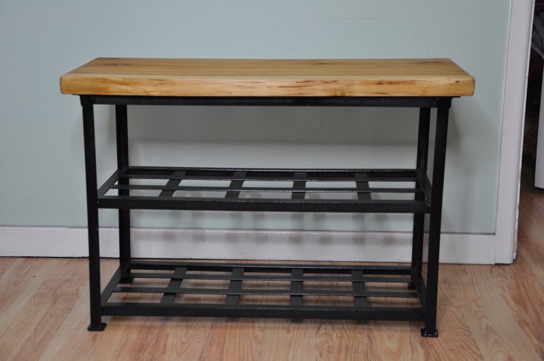 May include: A black metal shoe rack with two shelves and a wooden top. The shelves are made of a black metal grid.